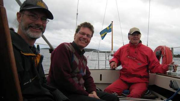 Foto på tre glada män i sittbrunn på båt under 24-timmarssegling.